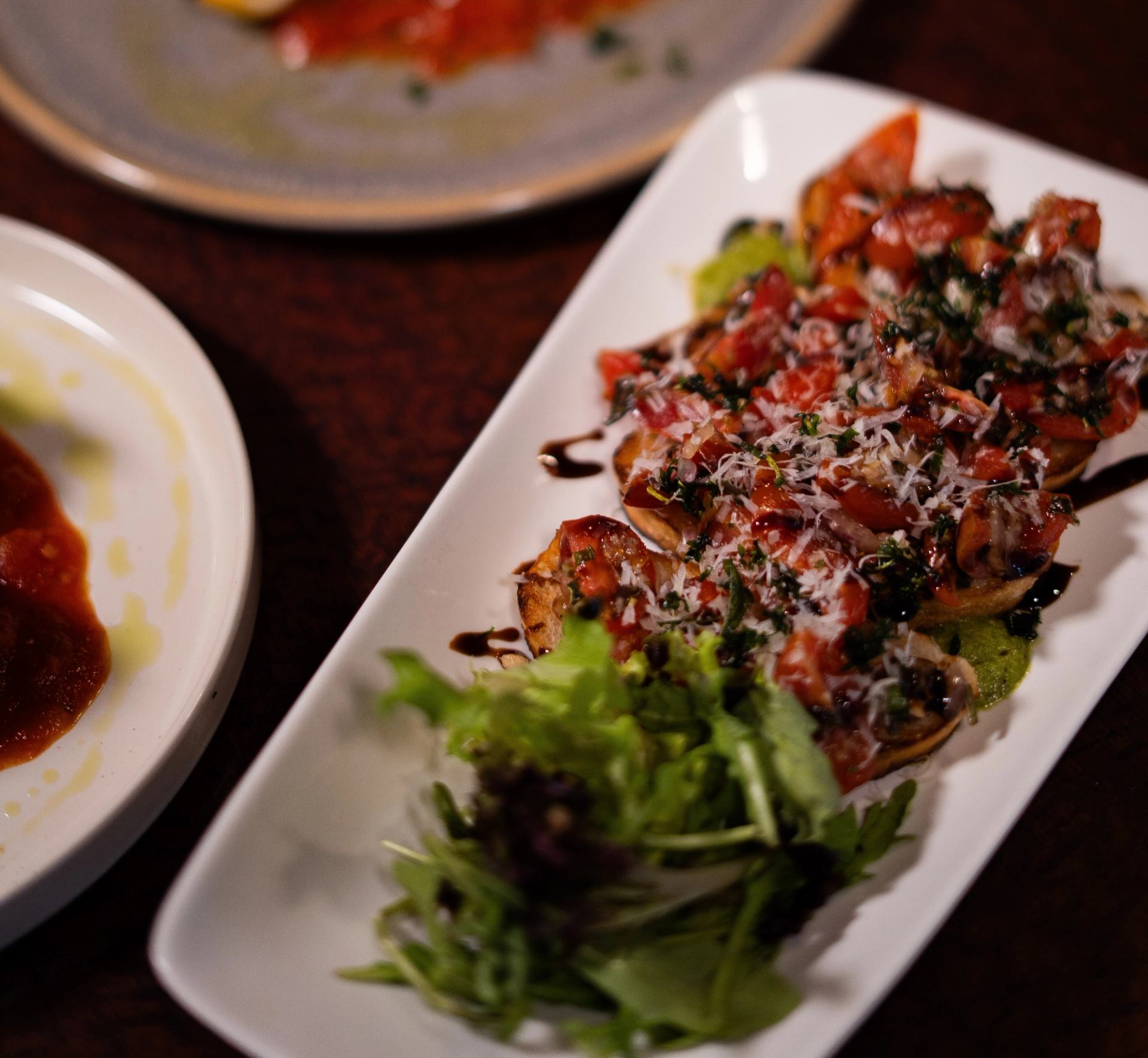 Rectangular plate of bruschetta with chopped tomatoes, herbs, grated cheese and mixed greens.