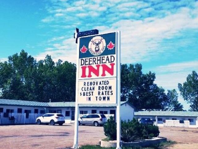 Deerhead Inn sign in front of hotel building with parked cars in a lot.