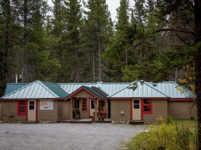 Rustic lodge with green roof and red windows, nestled in a forest of tall evergreens.