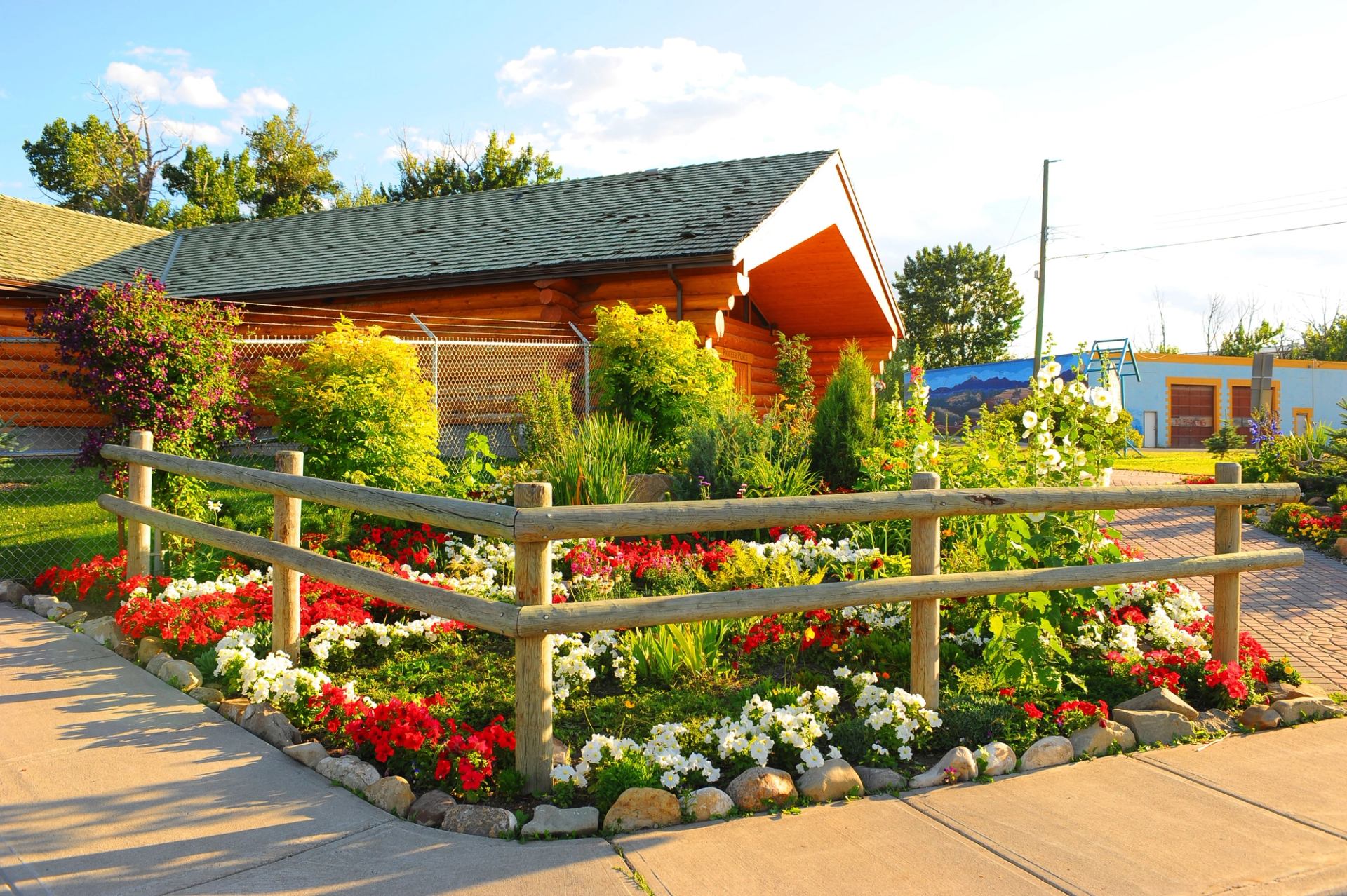 Flower garden in front of log cabin with green roof and wooden fence.