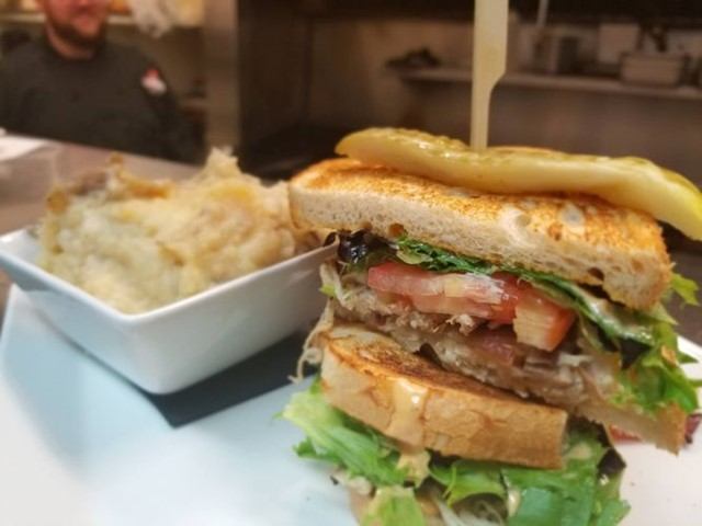 Gourmet sandwich with layers and creamy side dish in a kitchen setting.