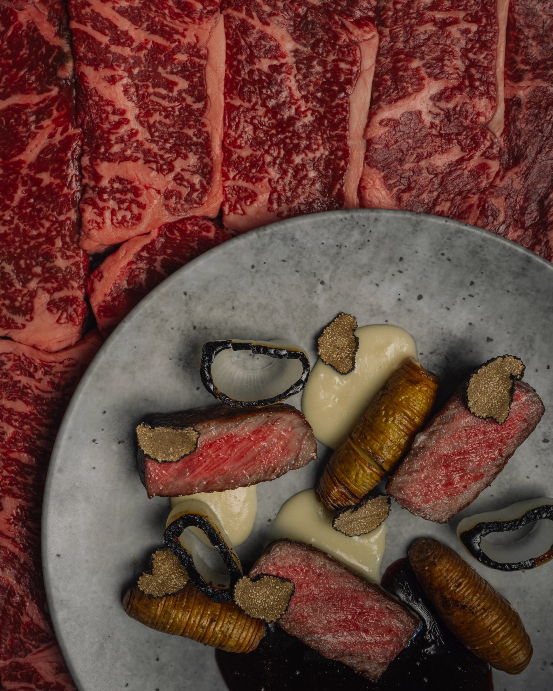 Plate of gourmet beef with truffle and crispy rolls, raw marbled beef in background.