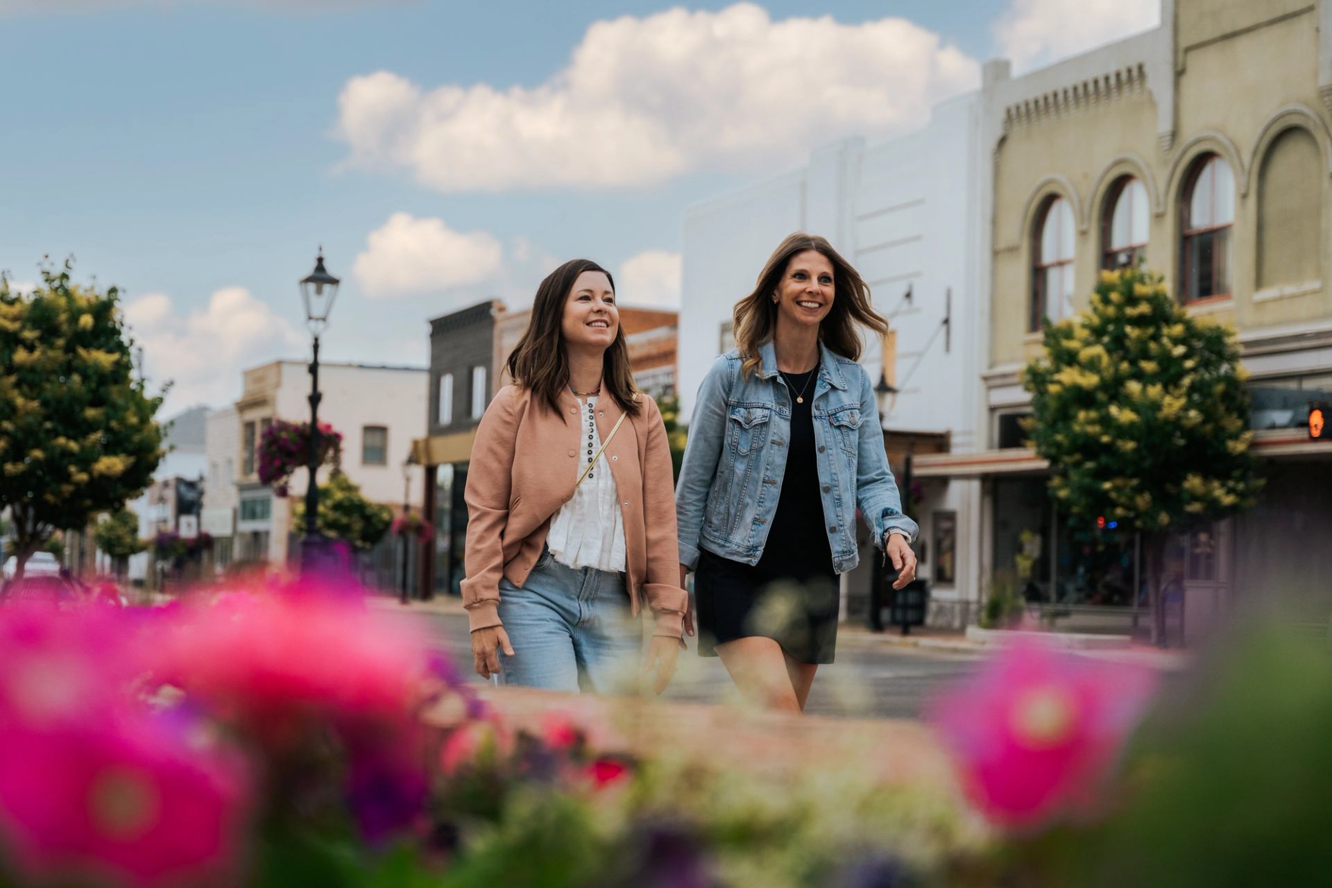 Two people walking through a colorful downtown street lined with shops and flowers.