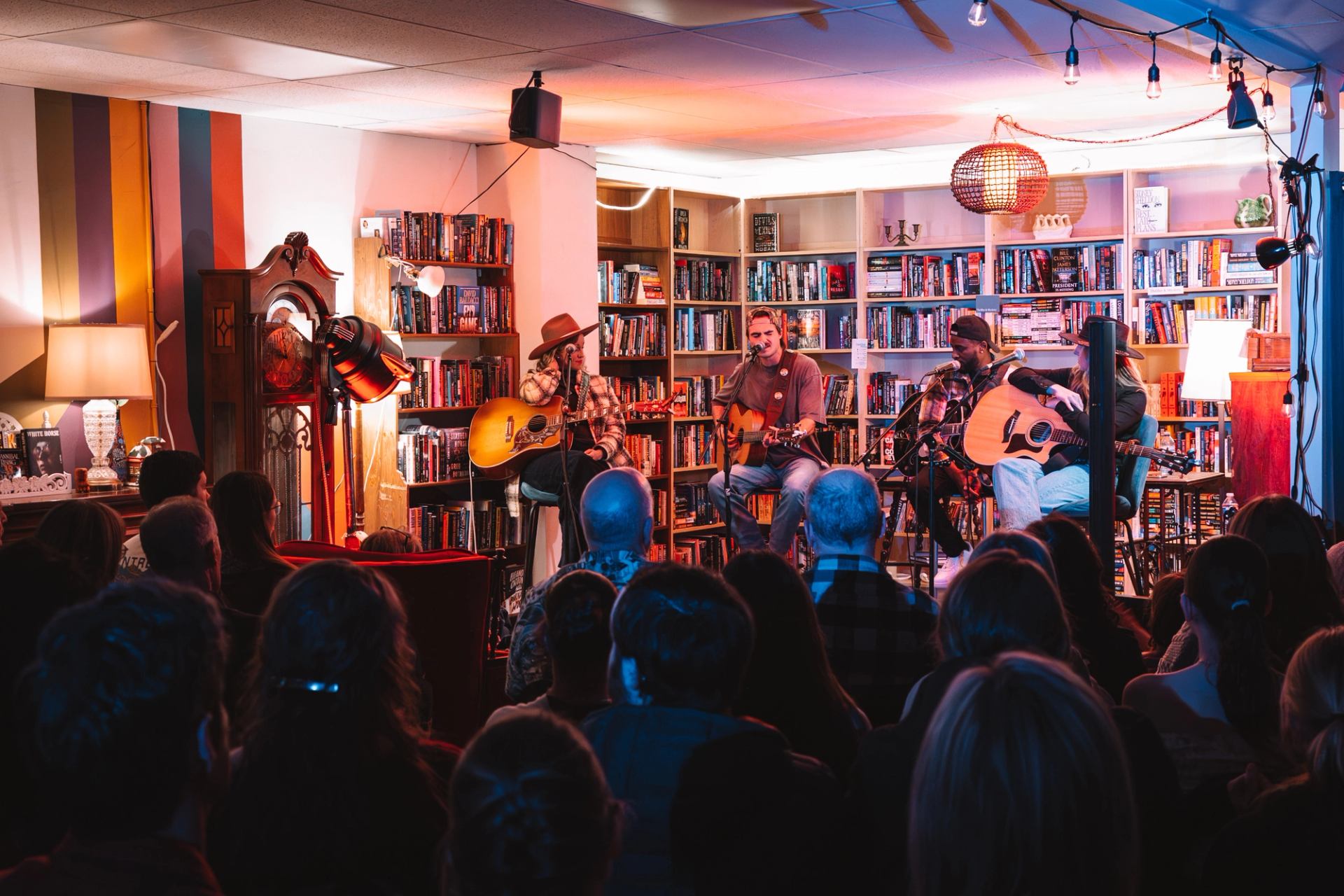 Musicians play acoustic guitars before a seated audience in a bookstore.
