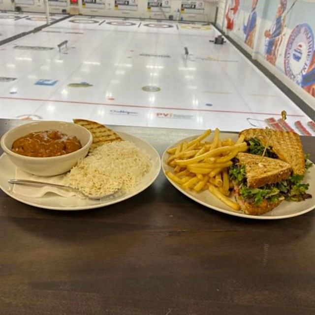 Plates of soup and sandwich with fries on table beside curling rink.