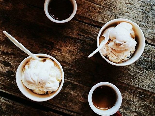 Bowls of ice cream and small cups of chocolate sauce on a wooden table.