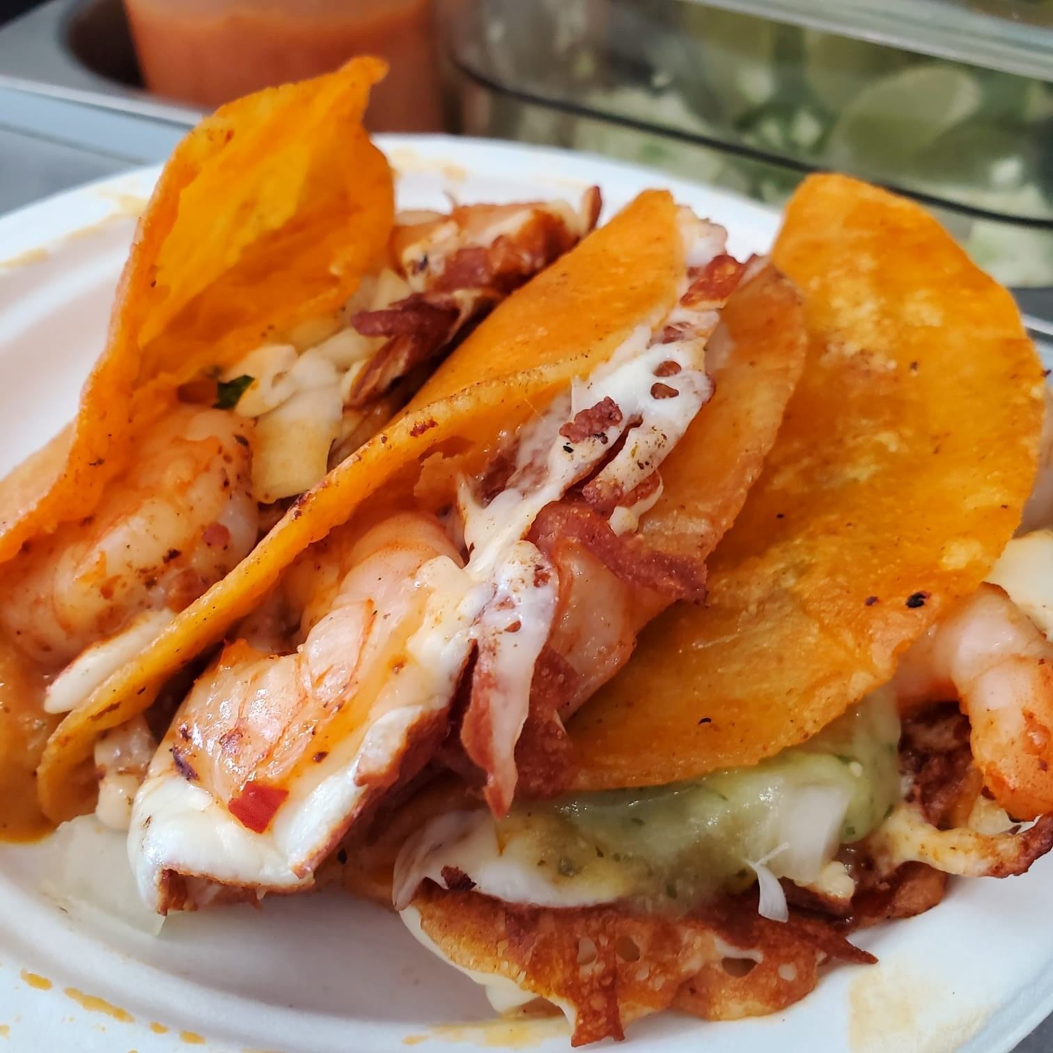 Close-up of shrimp tacos with melted cheese and salsa on a white plate.