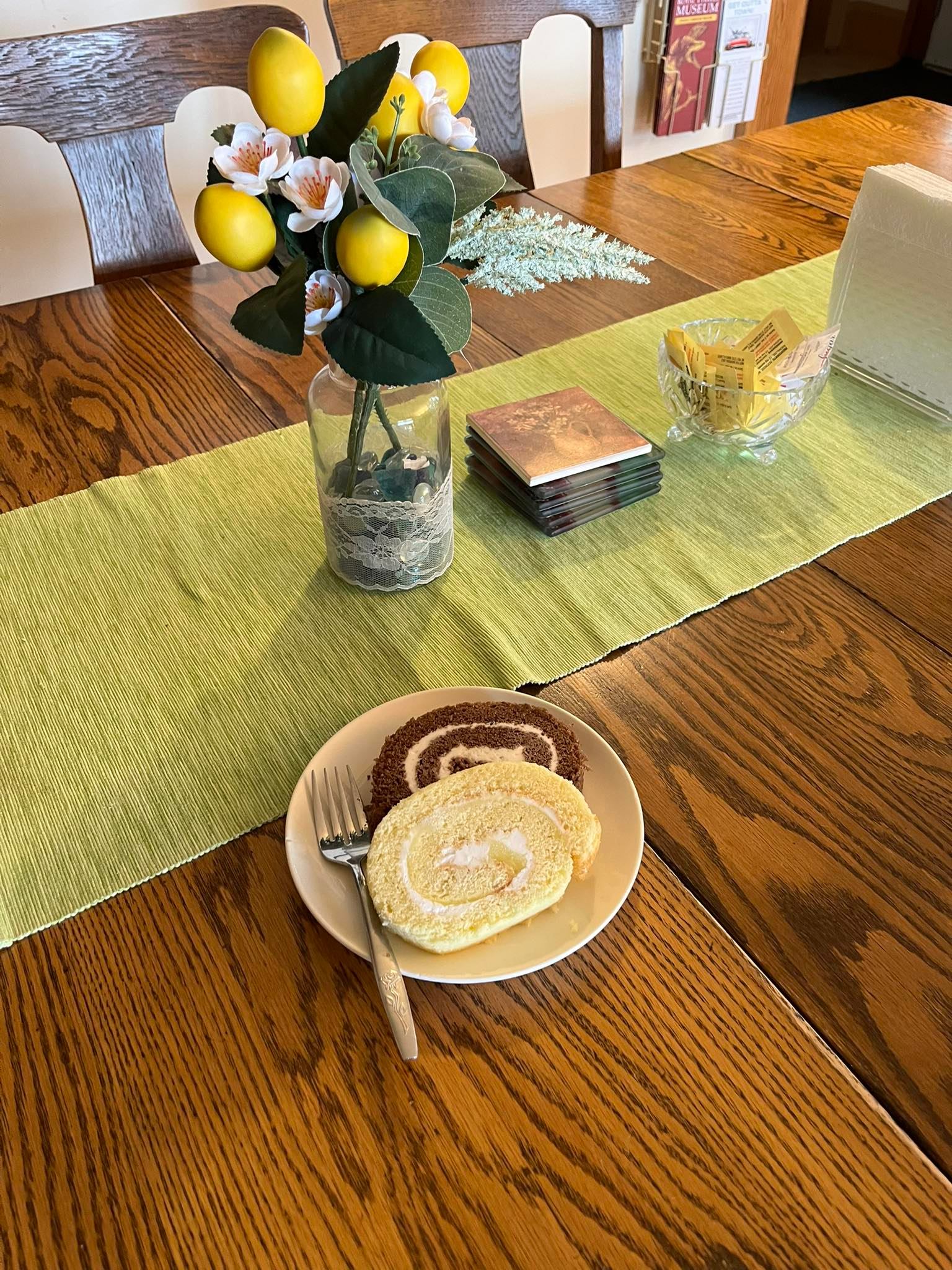Wooden dining table with cake slices on plate, lemon bouquet, coasters and napkins.