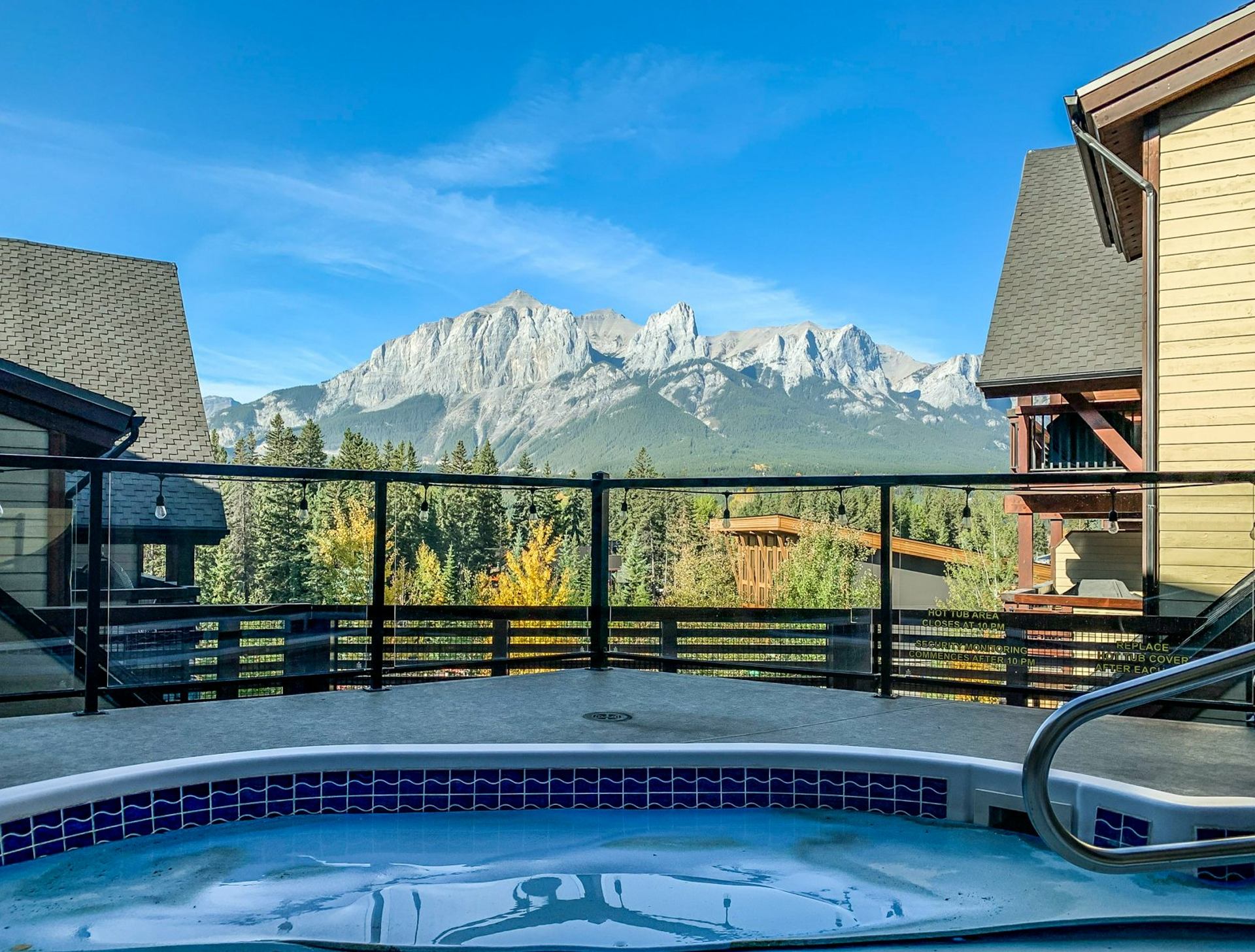 Outdoor hot tub on balcony overlooking forested valley and rocky mountain range.