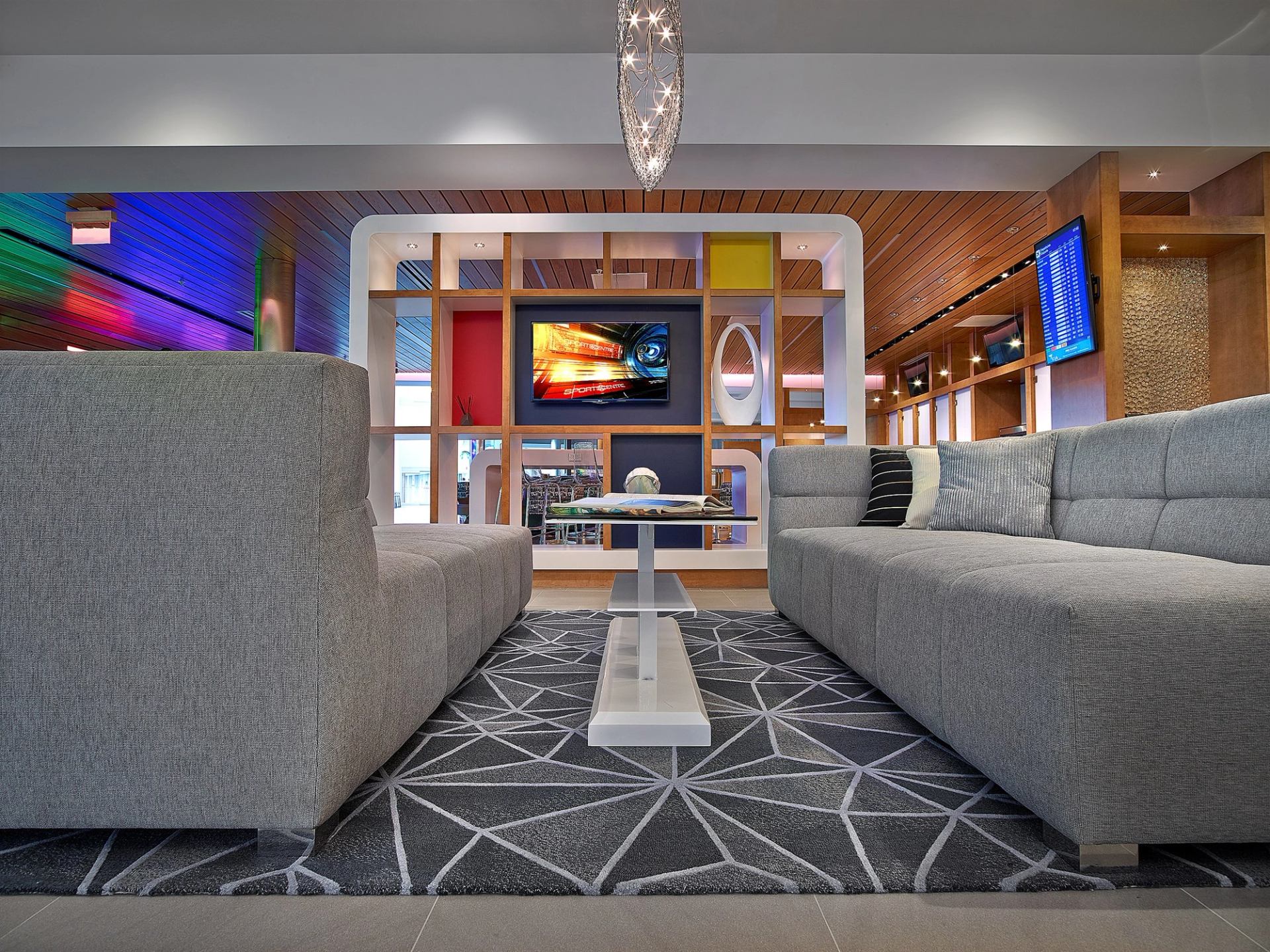 Modern lounge with grey sofas, geometric rug, and colorful shelving at HALO Bar|Bistro.