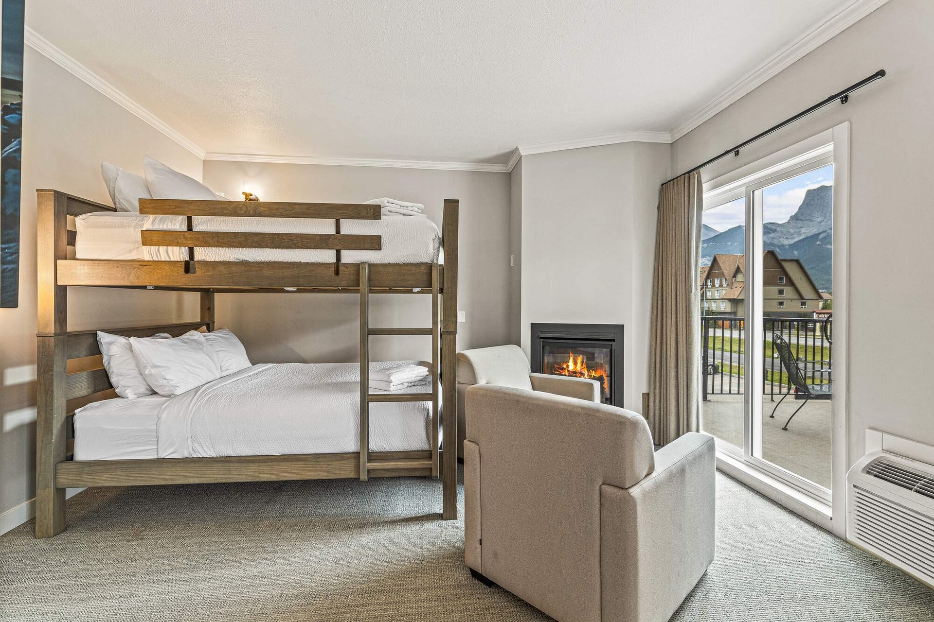 Hotel room with bunk bed, sofa by fireplace, and balcony doors with mountain view.