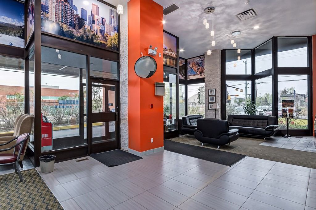 Bright hotel lobby with orange accent wall, modern seating, large windows, and city-themed décor.