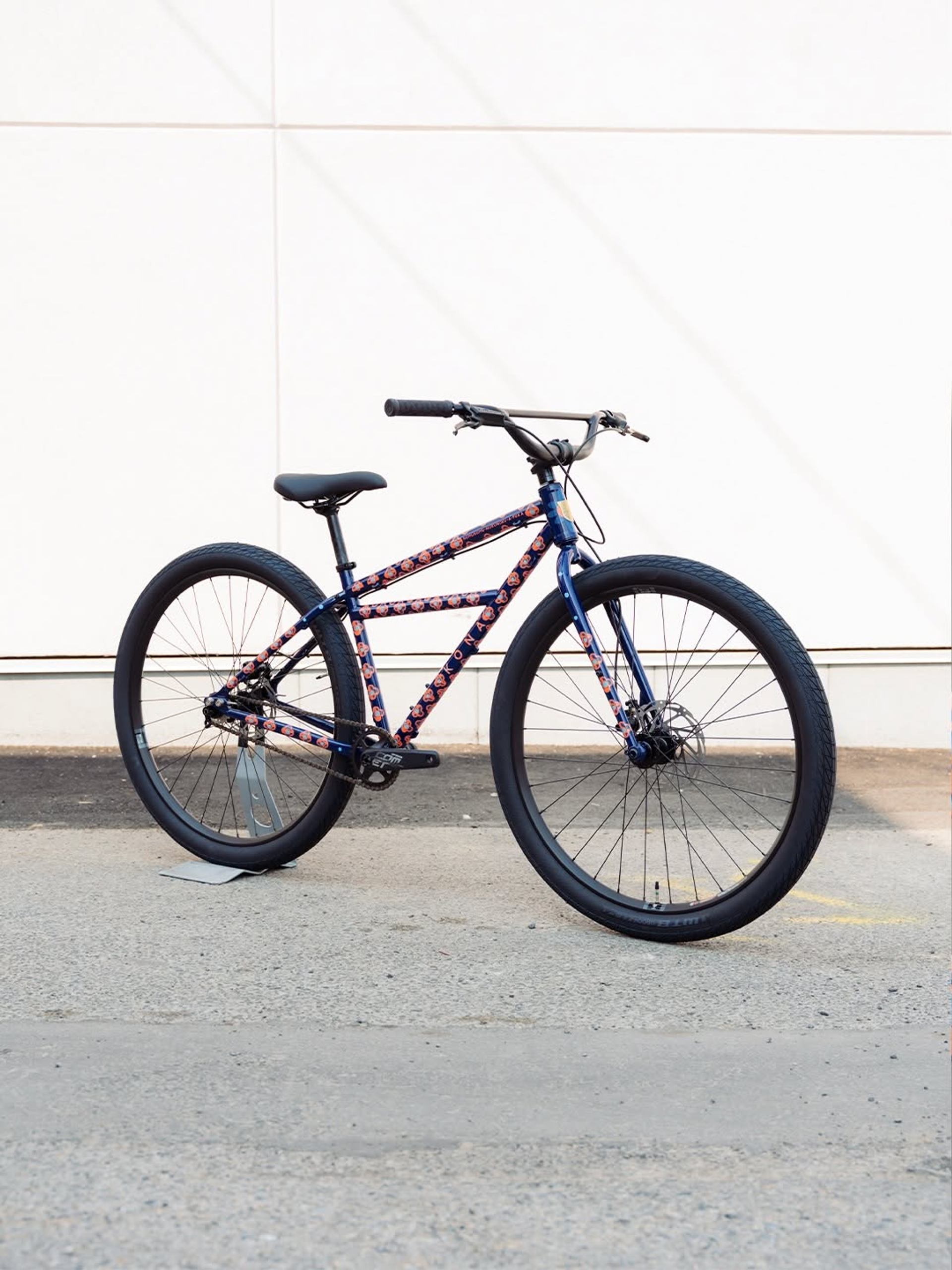 Blue floral-patterned bicycle with black tires stands against a white panelled wall.