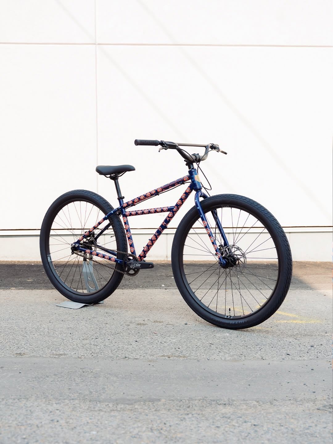 Blue floral-patterned bicycle with black tires stands against a white panelled wall.
