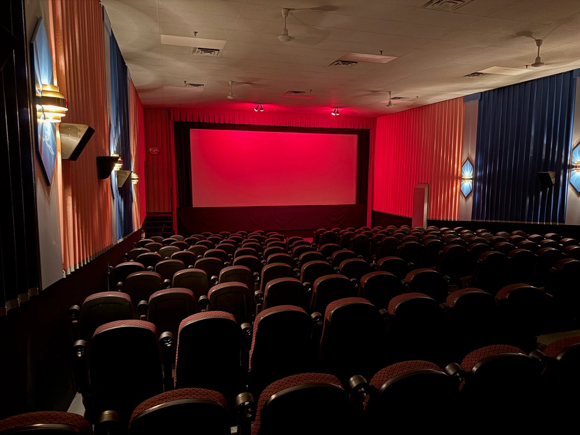 Empty movie theater with red lighting and rows of seats facing a large screen.
