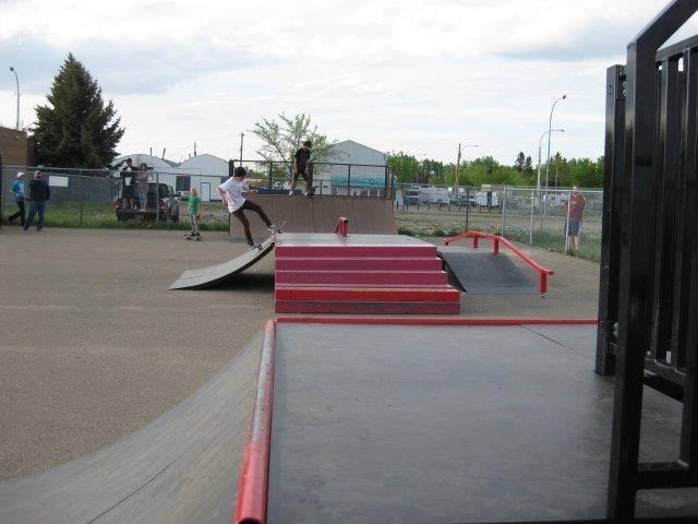 Skaters using ramps, rails, and platforms at an outdoor skateboard park.