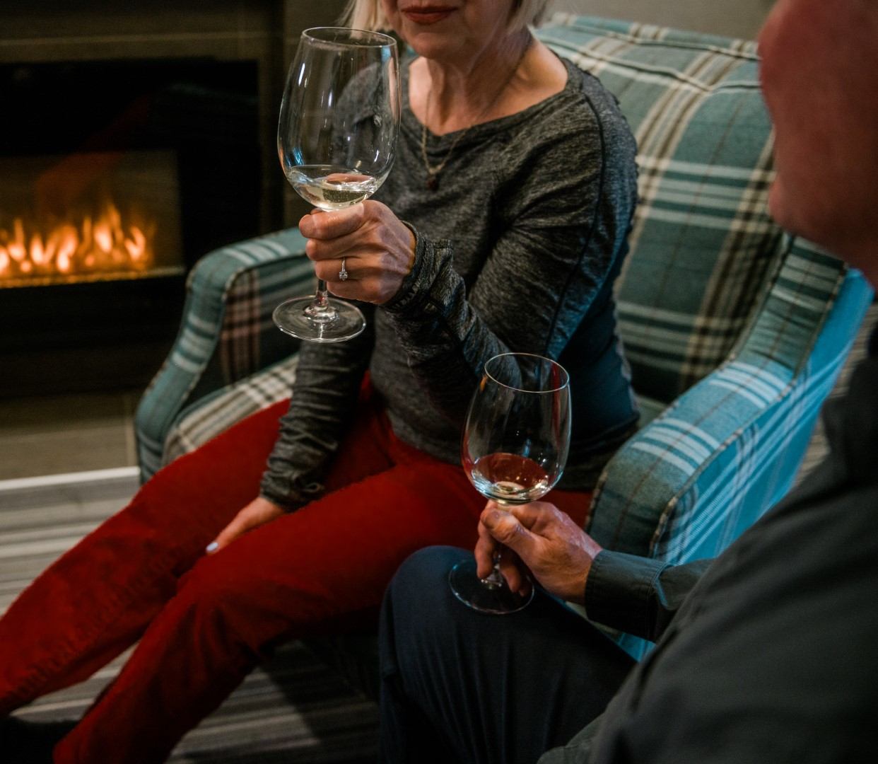 Two people sitting by a fireplace, enjoying glasses of wine in a cozy lodge setting.