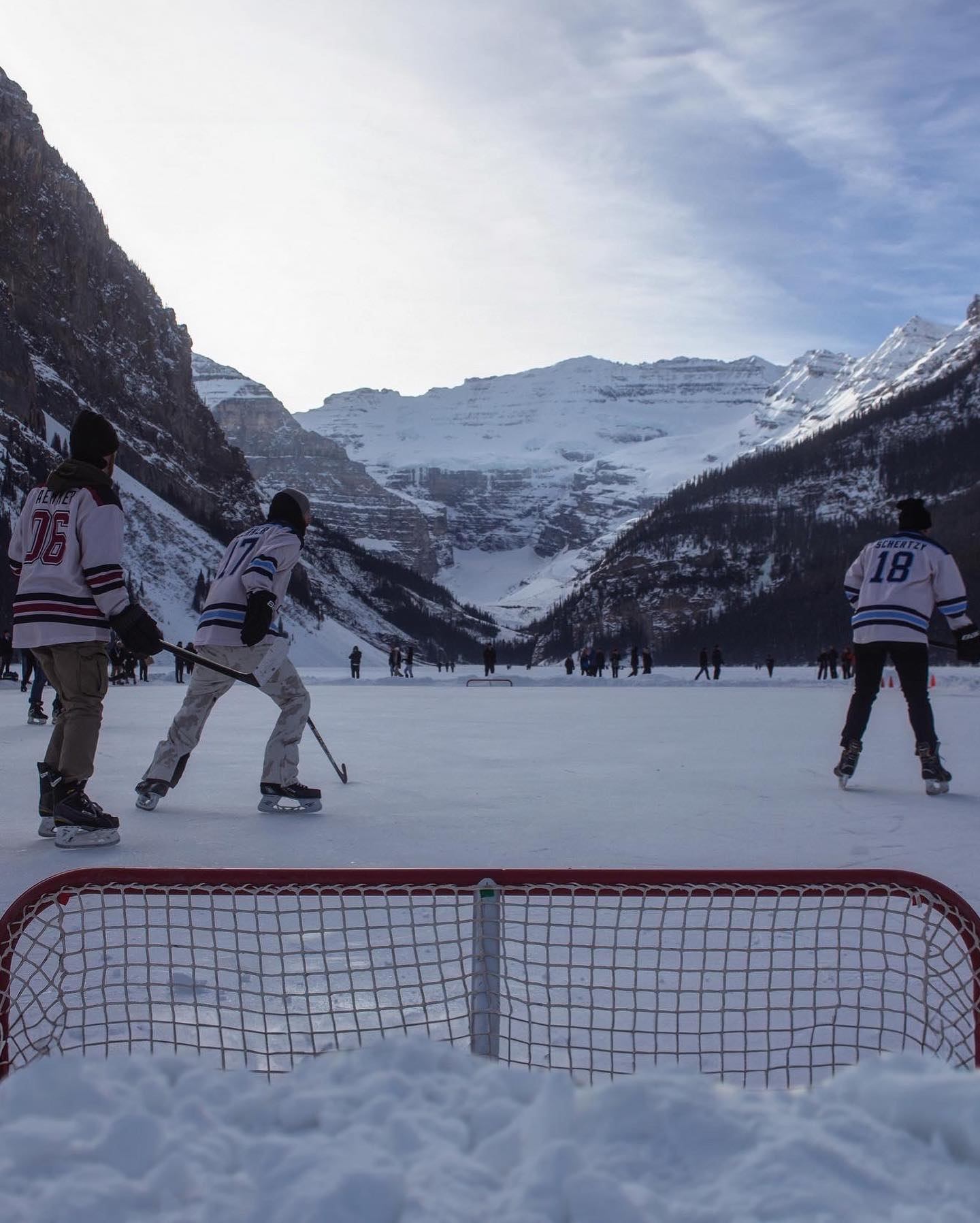 Players skating and playing hockey on an ice-covered lake with snowy peaks