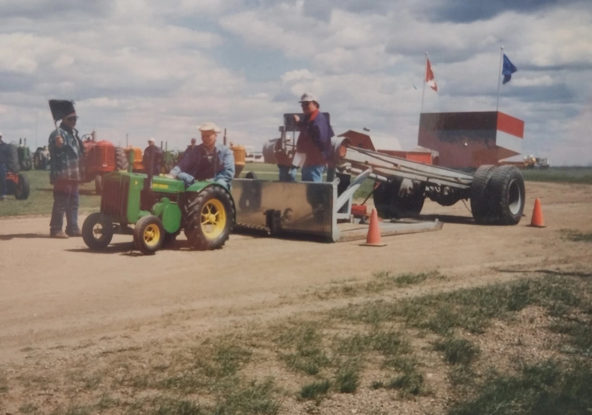 A tiny green tractor in front of farm machinery.