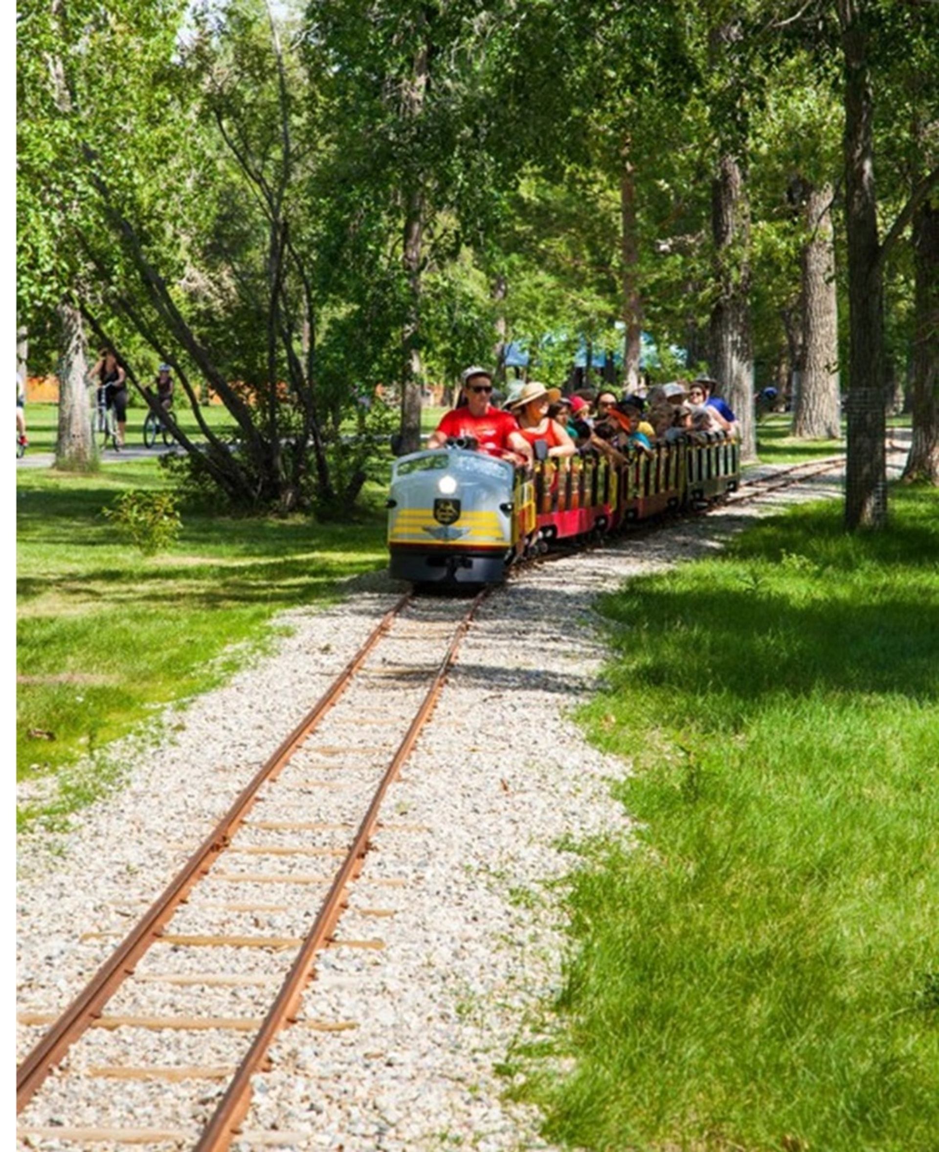 Miniature train with passengers riding through greenery at Bowness Park