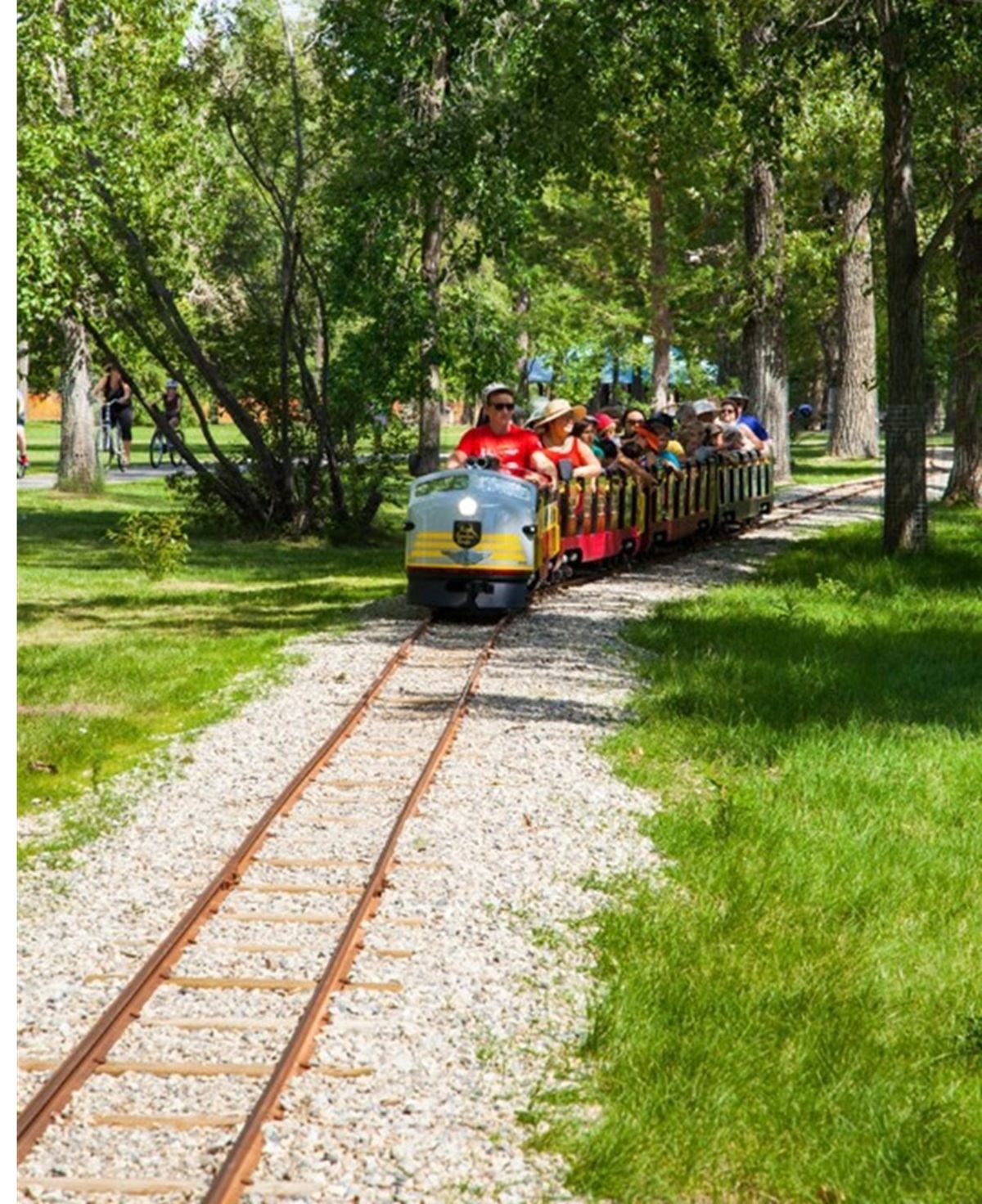 Miniature train with passengers riding through greenery at Bowness Park