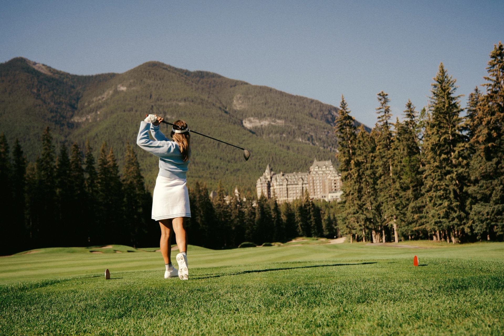 Golfer teeing off at Fairmont Banff Springs Golf Course with mountain backdrop and forest views.