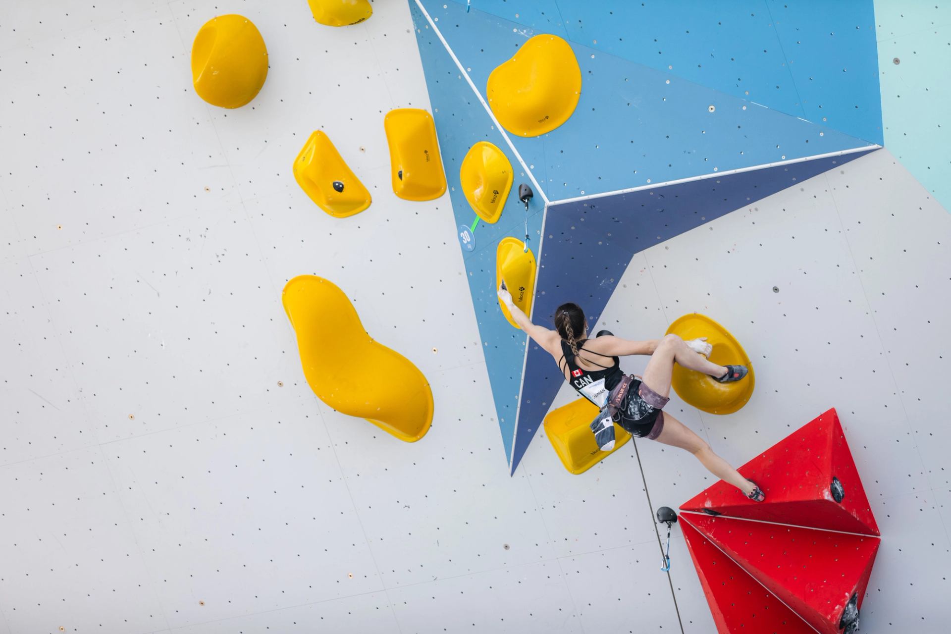 A female climber reaches for a yellow hold on a multi-colored indoor climbing wall.