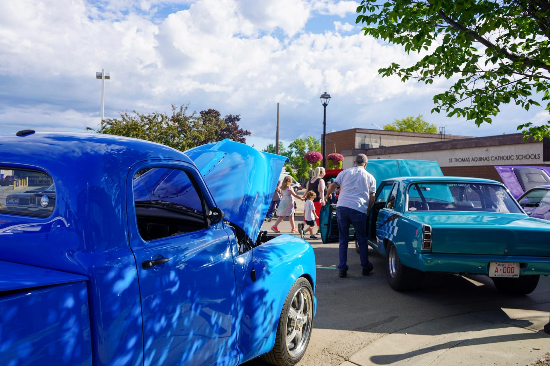 Classic blue cars with open hoods at outdoor show near St. Thomas Aquinas Catholic Schools.
