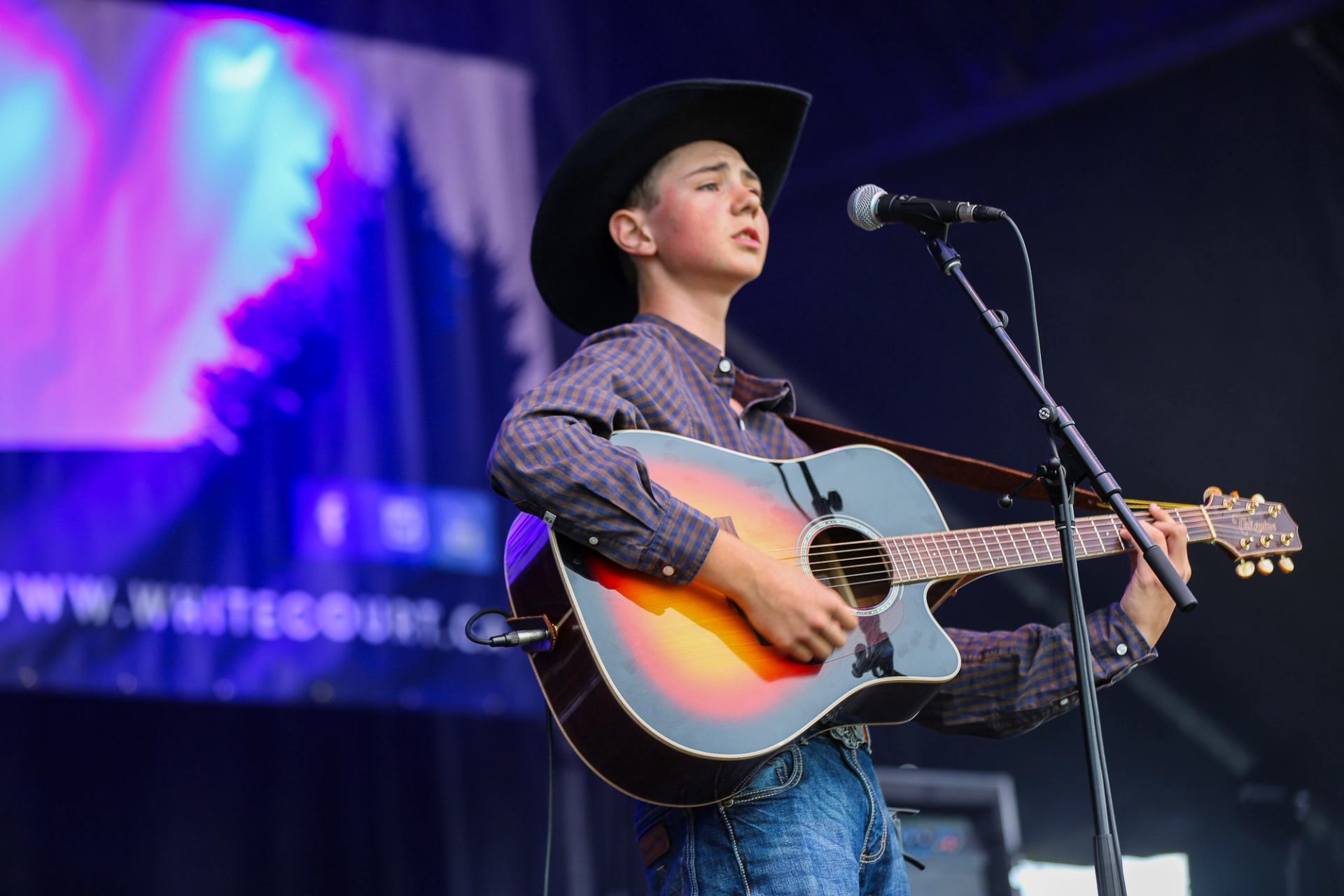 Musician in a cowboy hat playing acoustic guitar onstage.