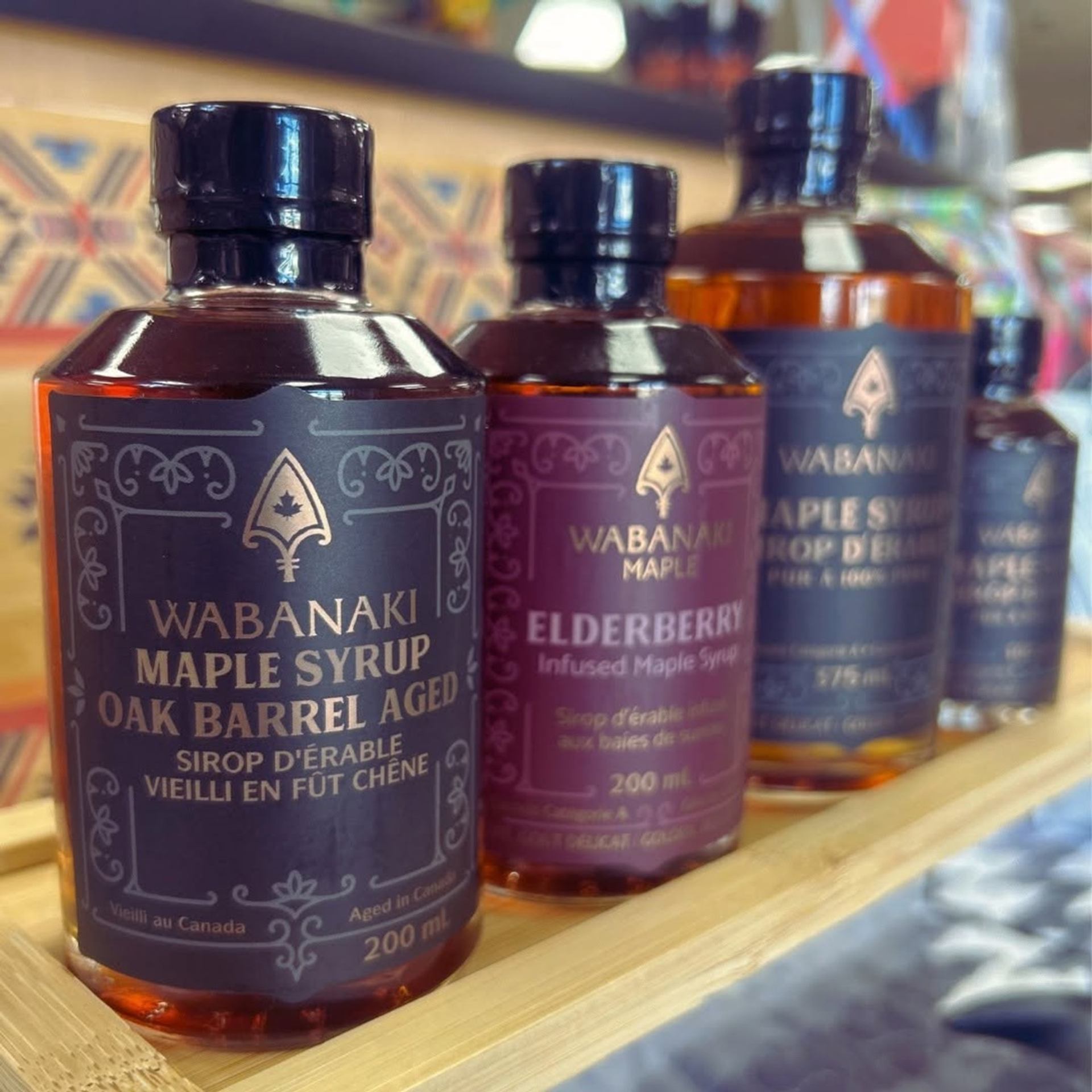 Wabanaki maple syrup bottles, including oak barrel aged and elderberry infused varieties, on shelf.