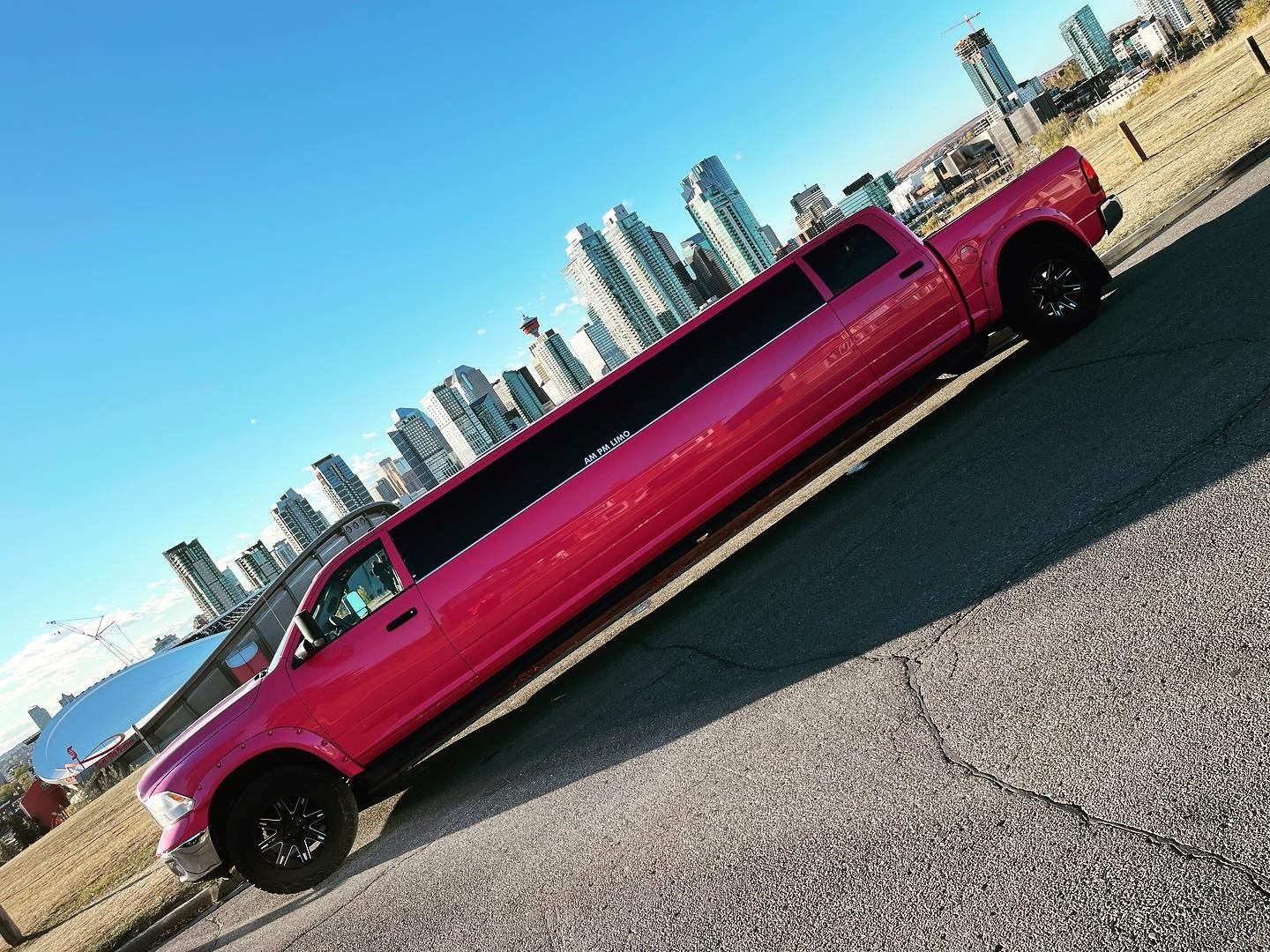 Bright pink stretch limo truck parked on city street under clear blue sky.