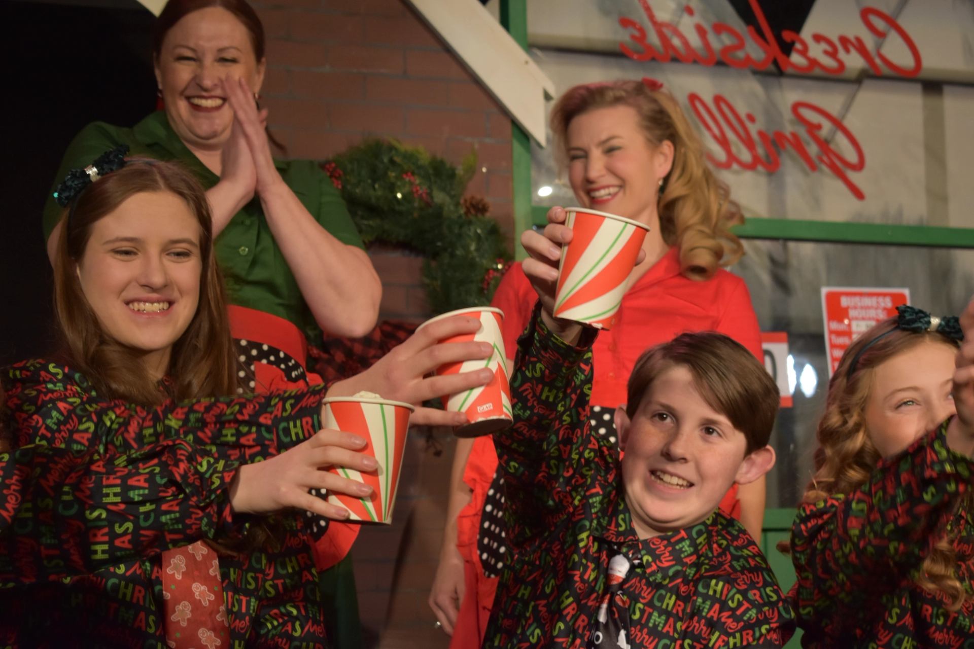 Group of people in festive clothing raising striped paper cups indoors.