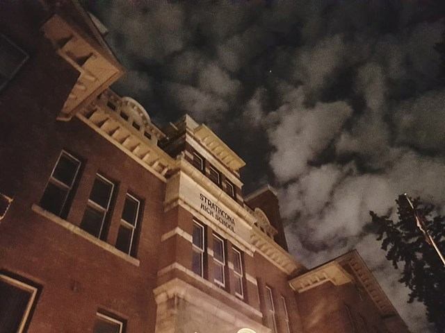 Brick high school building at night under cloudy sky, viewed from low angle.