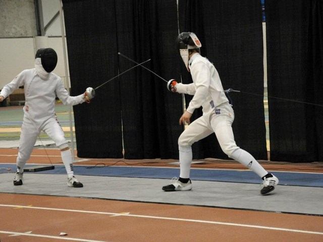 Fencers in white protective gear holding foils on an indoor piste.