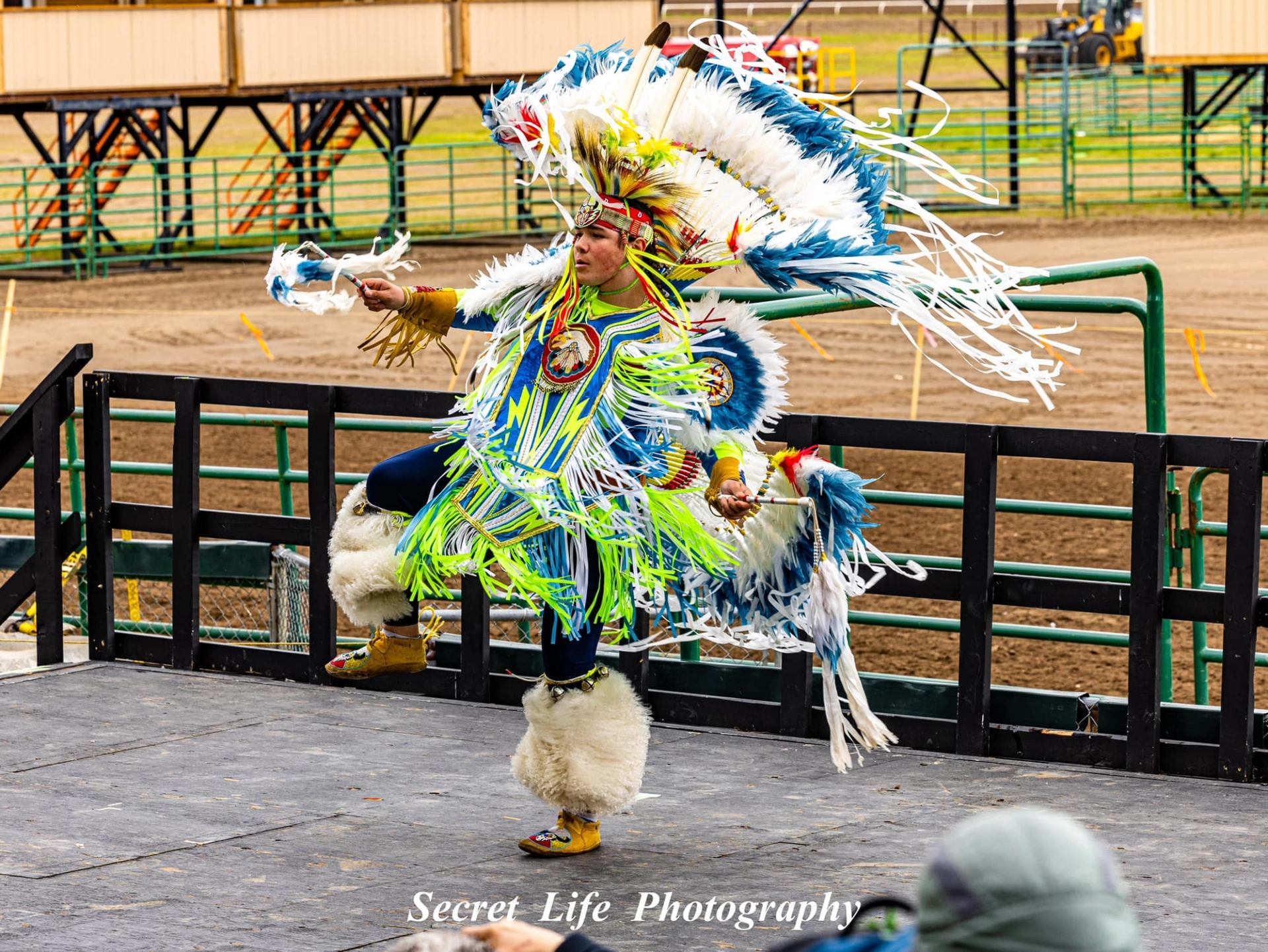 Performer in bright regalia dancing on a stage with fringe in motion.