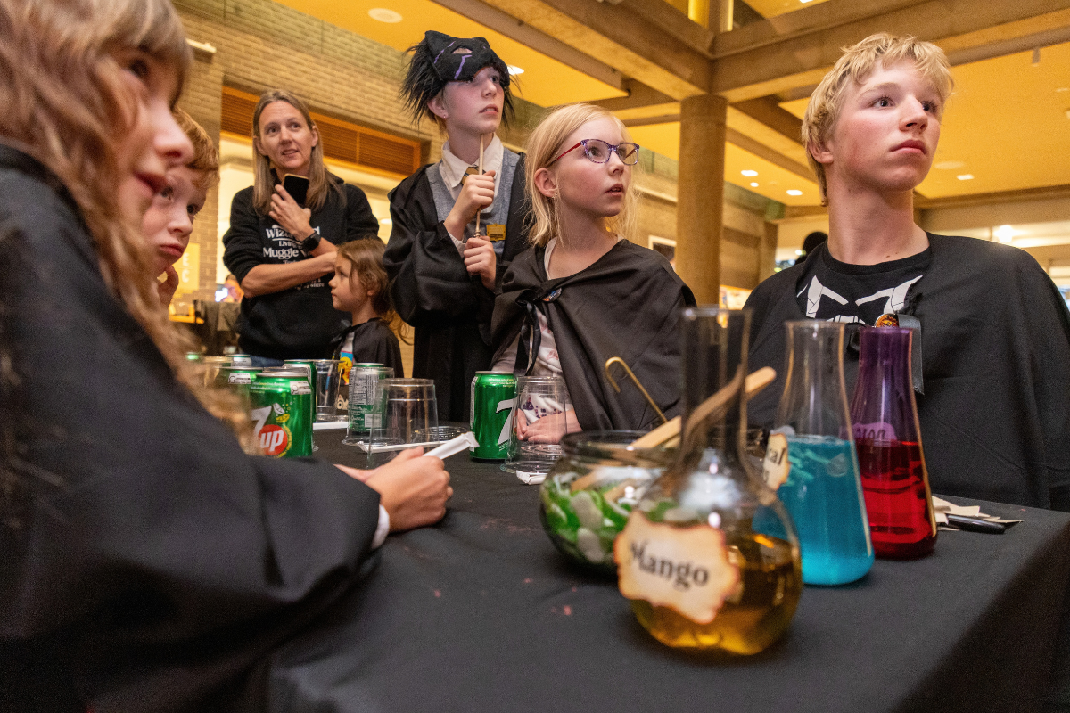 Costumed group gathers around a table with colourful drinks and potion jars.