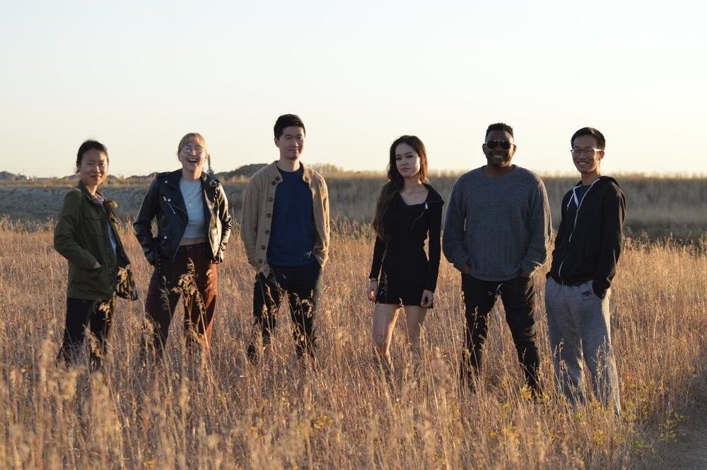 Group of six people standing in a tall grassy field under clear sky.
