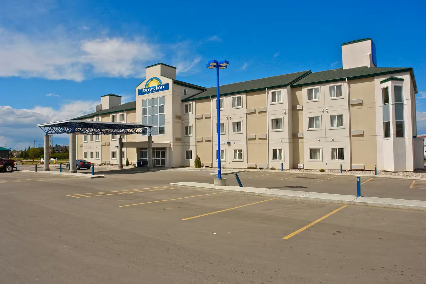 Days Inn Stony Plain exterior with covered entrance, guest parking, blue sky, and modern hotel design.