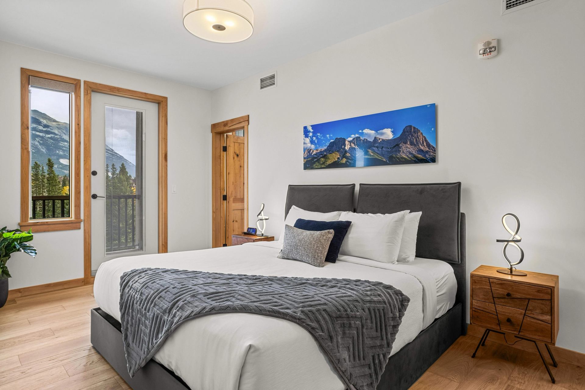 Bedroom with a large bed, wooden nightstands and mountain views through windows.