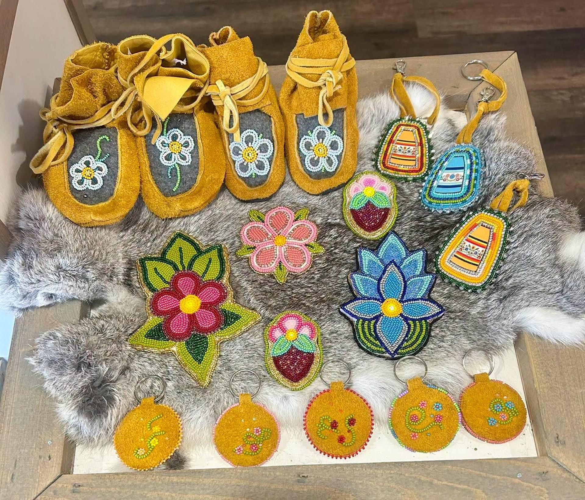 Beaded moccasins and colourful floral keychains displayed on a fur-covered wooden table.