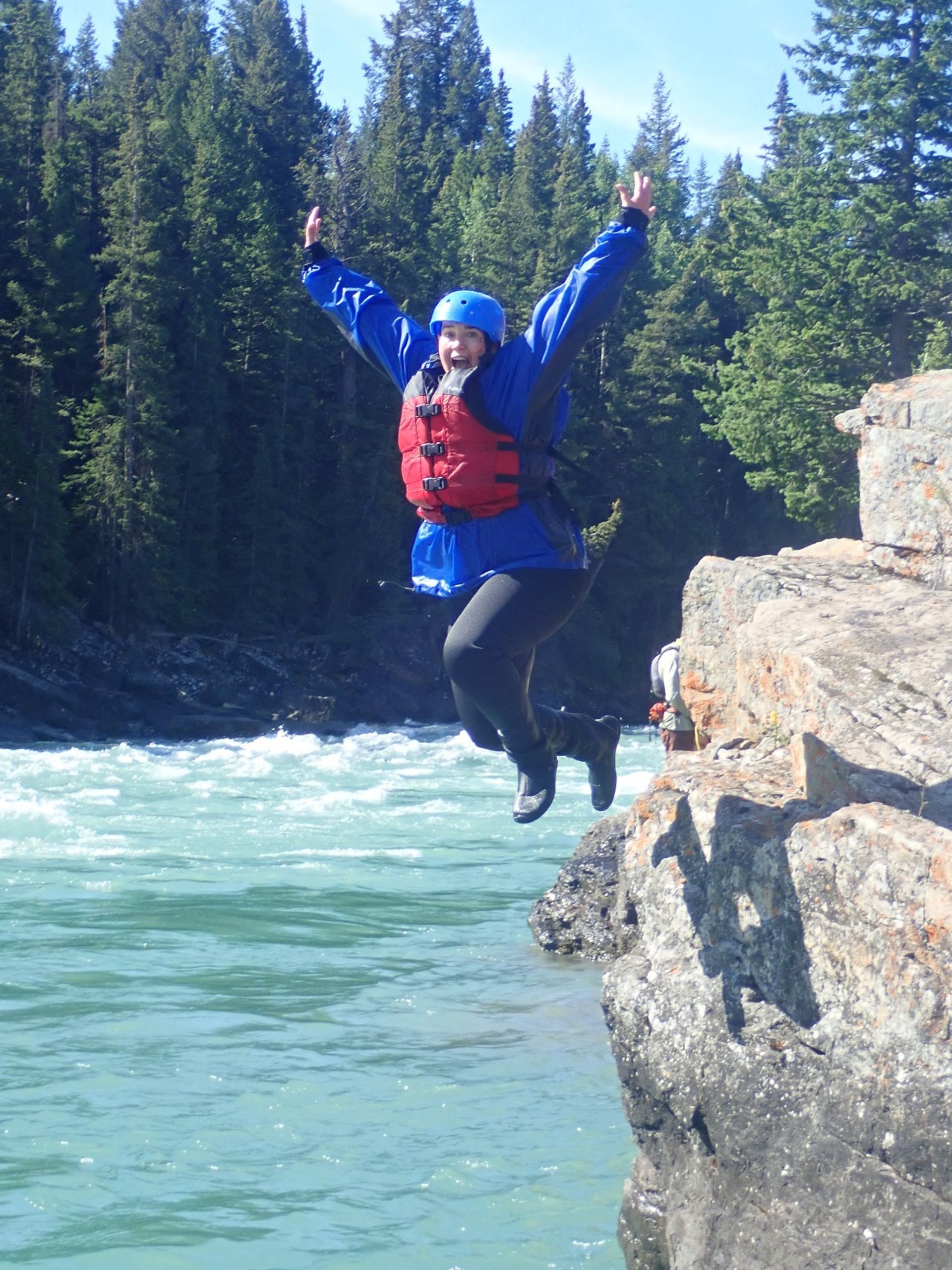 Person in helmet and life jacket jumps from rocky ledge into turquoise river.