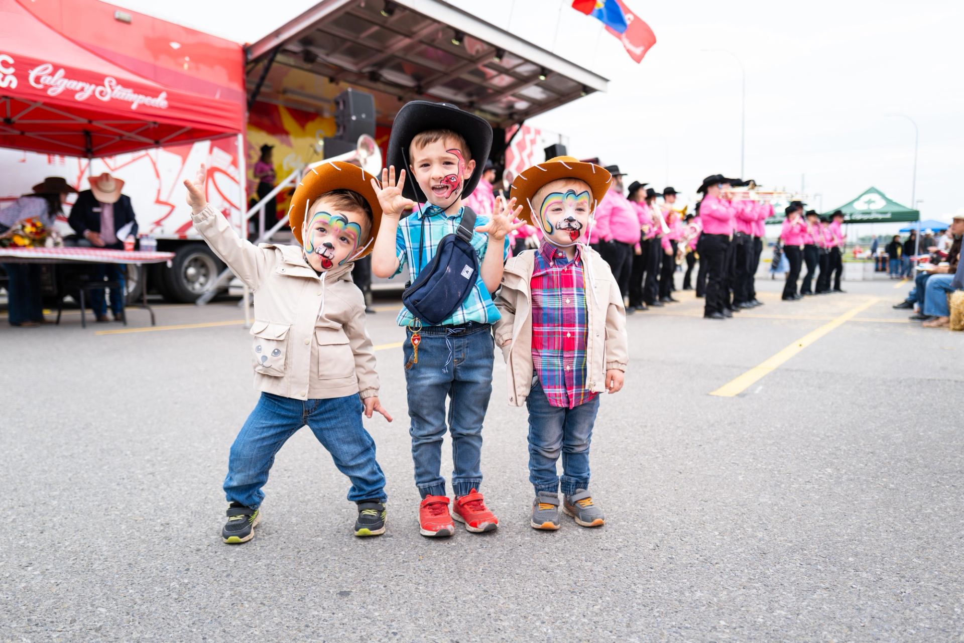 Children wearing cowboy hats and face paint pose in front of stage at Stampede Round Up.