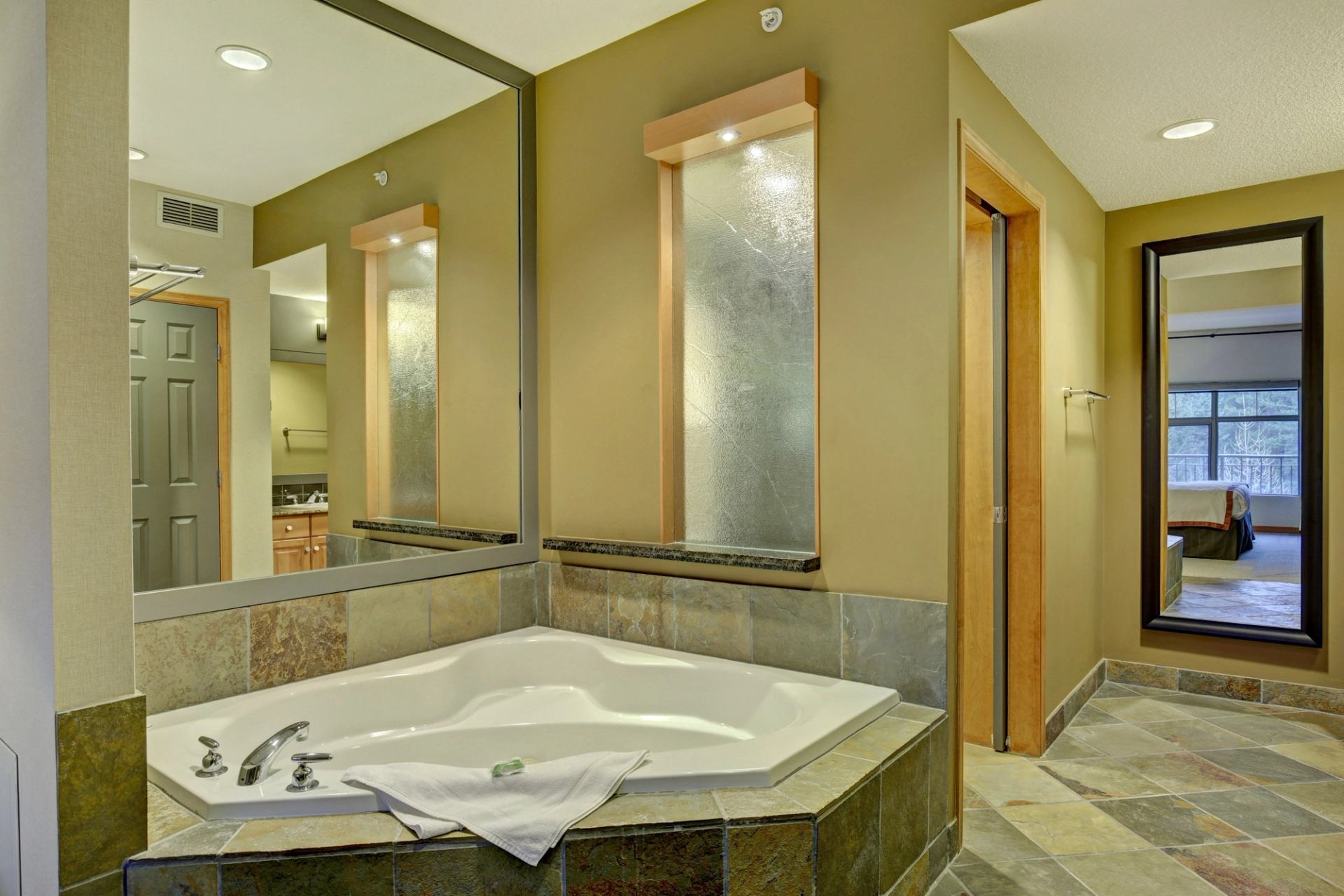 Bathroom with large corner soaking tub, mirrors, and stone tile accents.