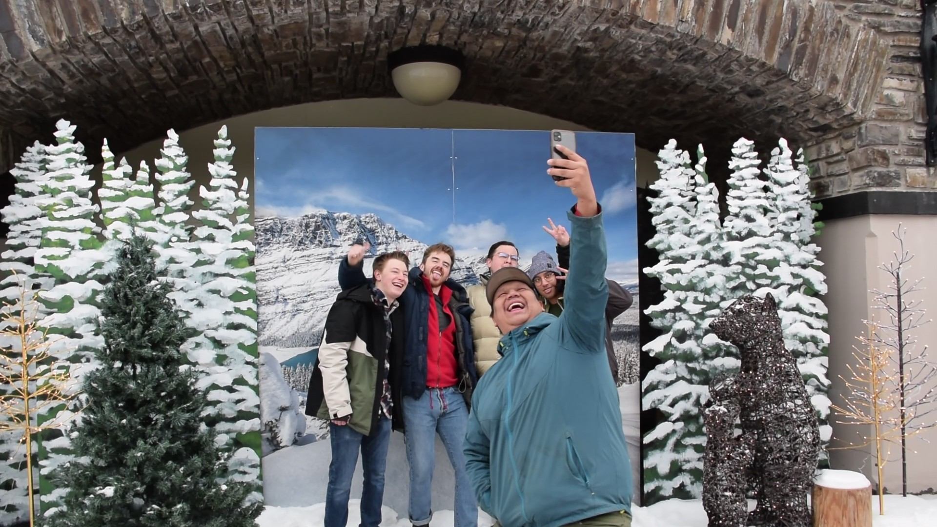 Group posing for a selfie in front of a snowy winter backdrop with decorated trees.