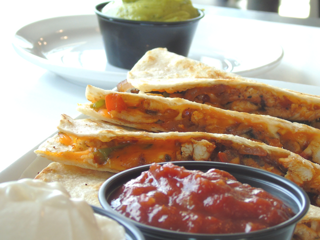Breakfast sandwich with tomato sauce, orange fillings, and a side bowl on a plate.