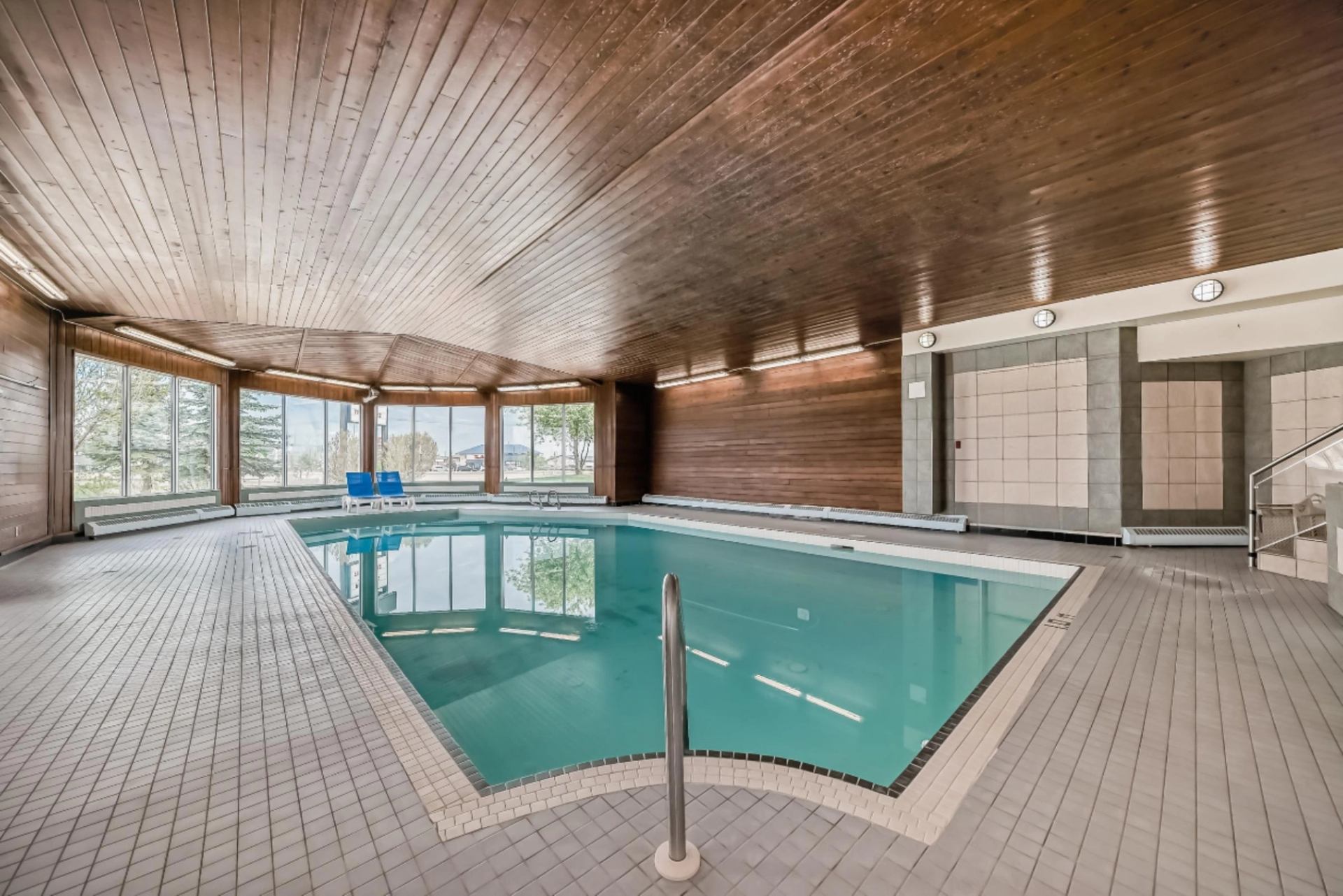 Bright indoor pool area with wood-paneled ceiling and large windows overlooking trees