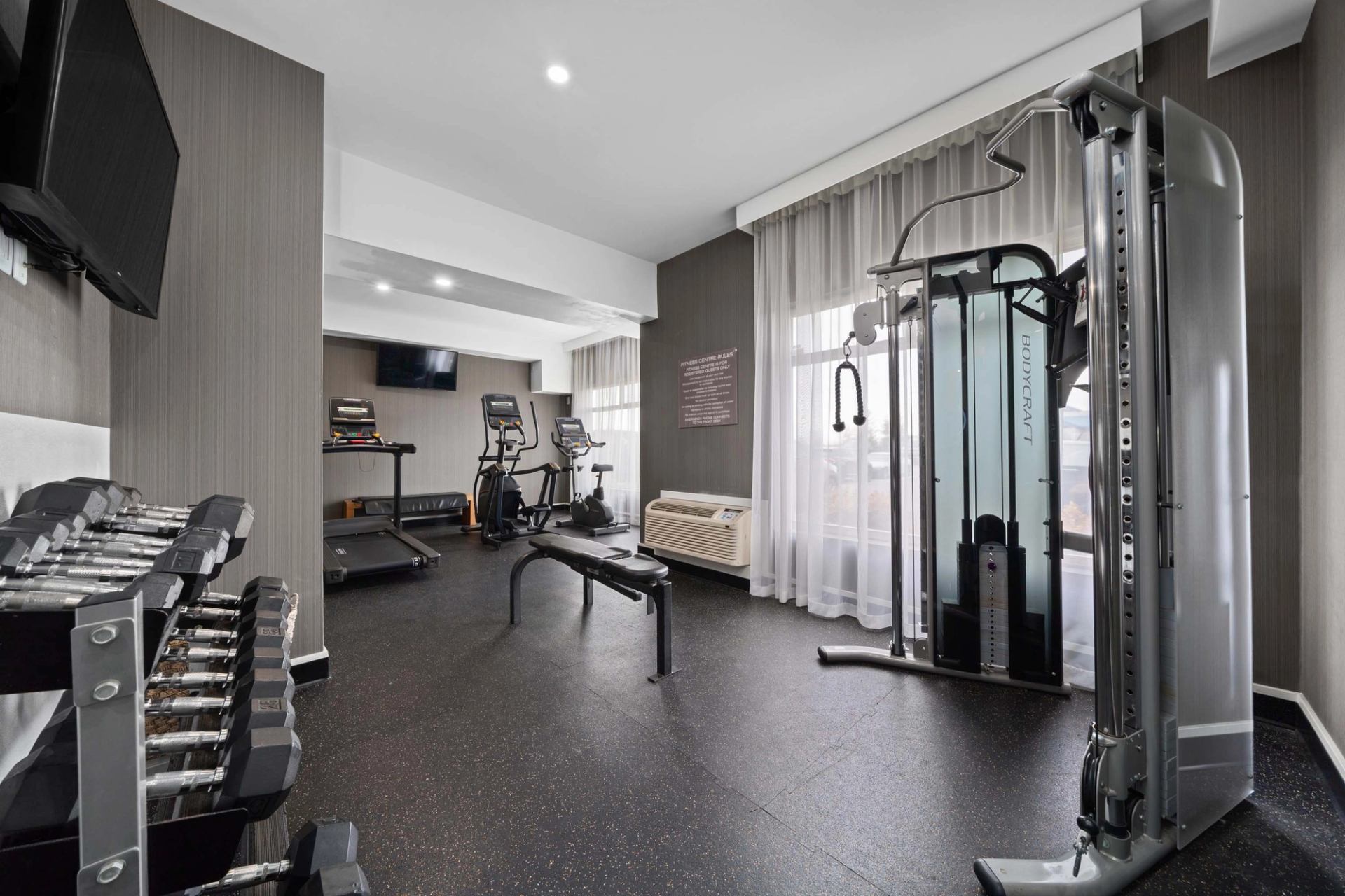 Hotel fitness room with dumbbells, bench, cardio machines, cable station and televisions.
