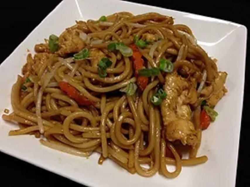 Stir-fried noodles with chicken, vegetables, and fresh green garnish.