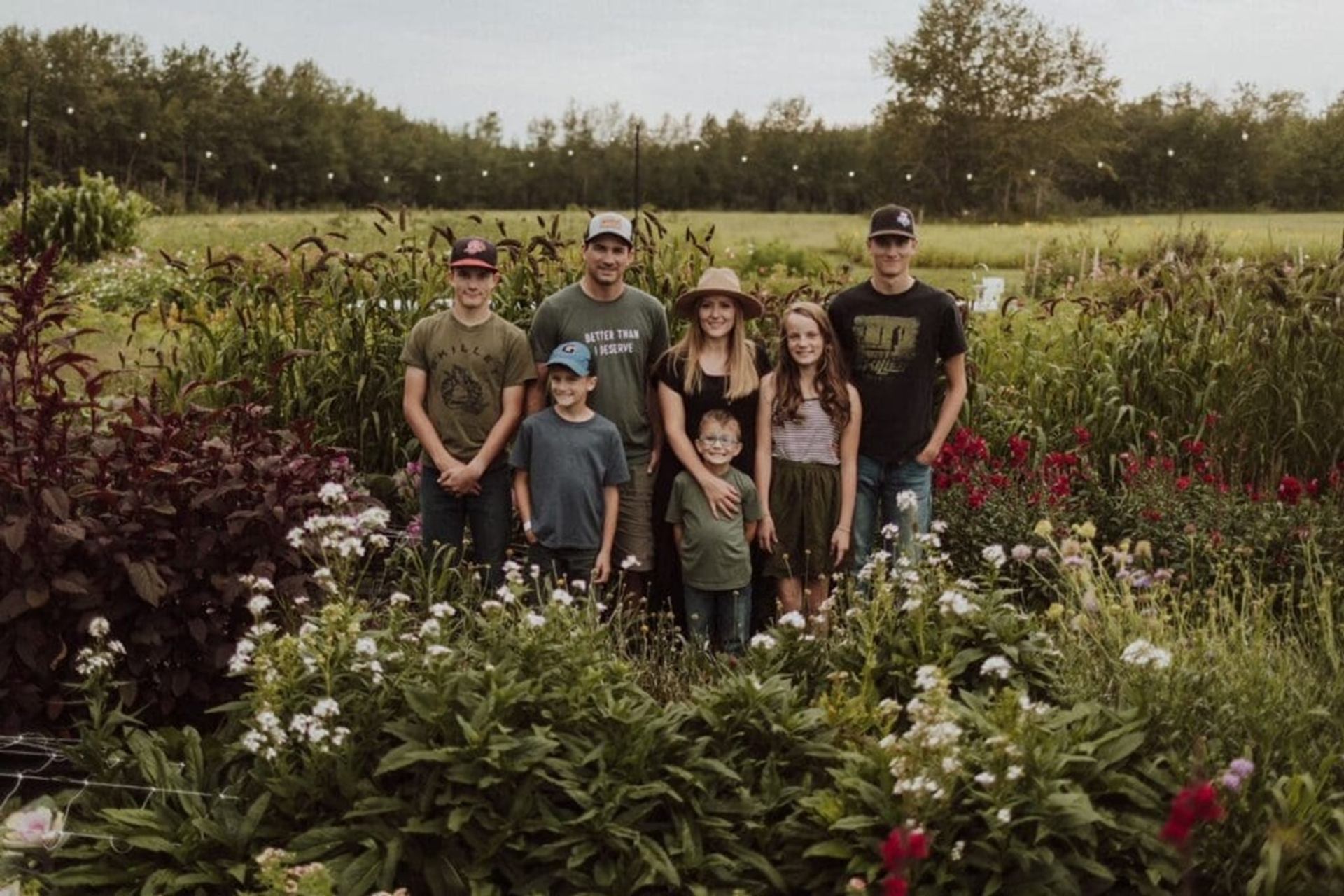 Group of seven people standing in a lush flower garden with fields behind.