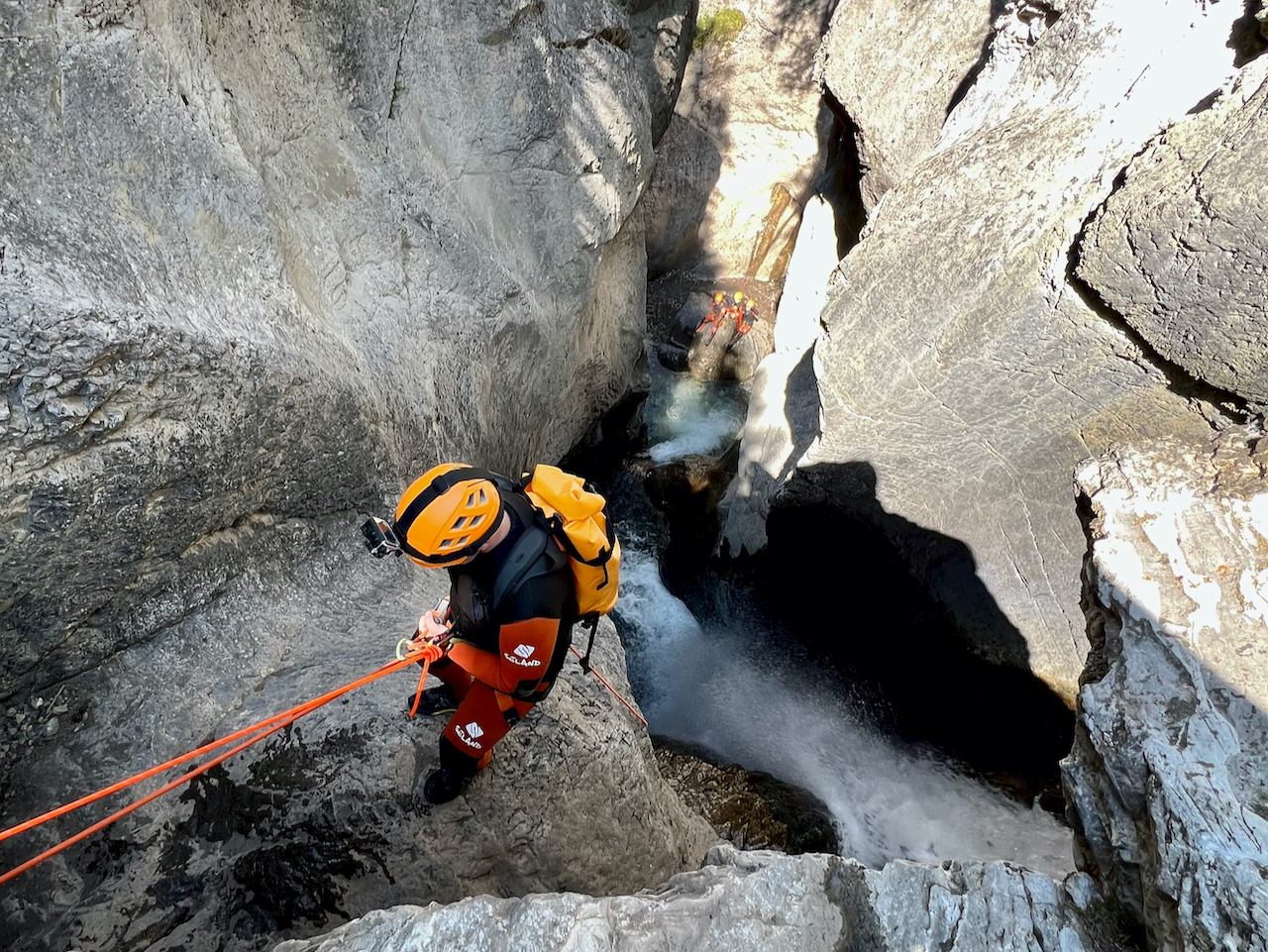 Adventurer rappelling on wet rock wall beside a cascading waterfall in Heart Creek.